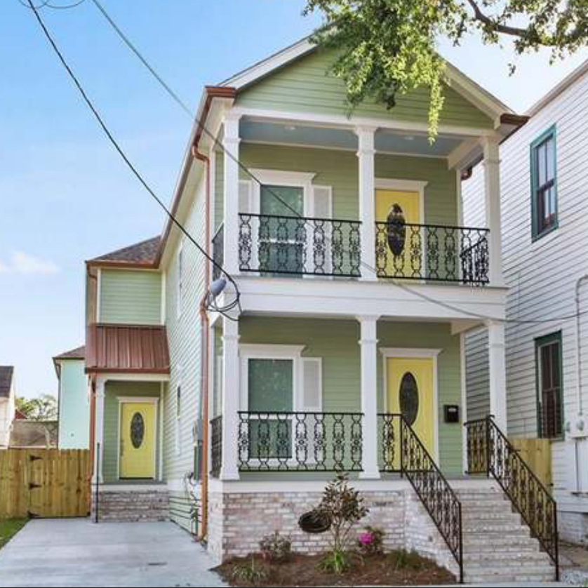 Renovated green double-gallery home with yellow doors and wrought-iron balconies in New Orleans